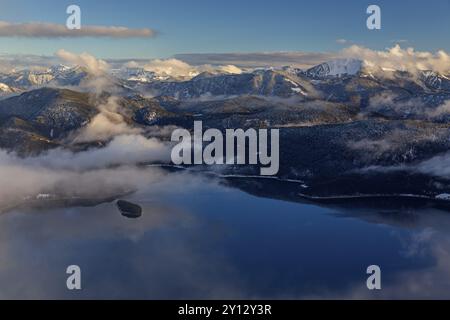 Vista lontana sul lago di montagna alla luce della sera, montagne innevate, nuvole e nebbia, inverno, vista da Herzogstand a Walchensee, Baviera al Foto Stock