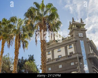 Moderna torre dell'orologio accanto ad alte palme, di fronte a un cielo blu brillante, tenerife, Isole canarie, spagna Foto Stock