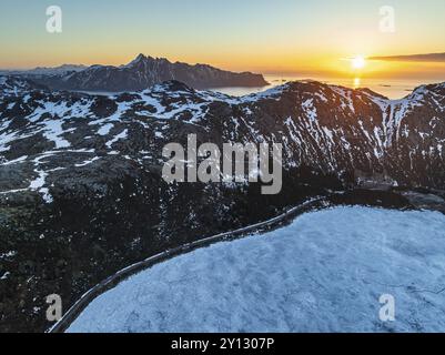 Vista aerea del lago ghiacciato di fronte a ripide montagne, costa, inverno, alba, Storvatnet, Flakstadoya, Lofoten, Norvegia, Europa Foto Stock