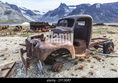 Auto arrugginite e tamburi di petrolio di fronte a ripide montagne, resti di una base aerea statunitense della seconda guerra mondiale, fiordo di Ikateq, Groenlandia orientale, Groenlandia, Nort Foto Stock