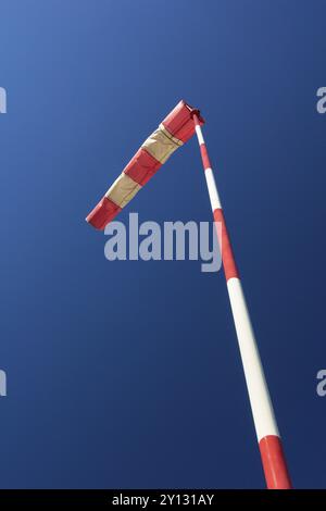 Una calza a vento rossa e bianca soffia contro un cielo azzurro limpido, la Germania, l'Europa Foto Stock