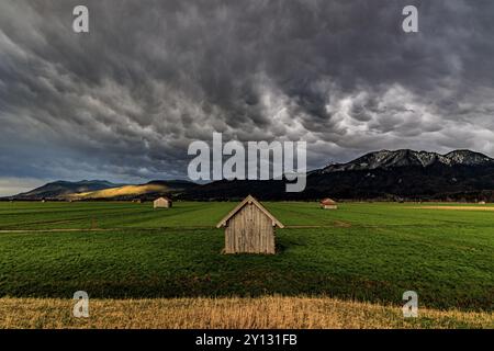 Piccola capanna in legno in un prato di fronte a un paesaggio montano, nuvole di tempesta, temporali, luce serale, Loisach-Lake Kochel-Moore, Baviera, Germania, Foto Stock
