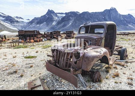 Auto arrugginite e tamburi di petrolio di fronte a ripide montagne, resti di una base aerea statunitense della seconda guerra mondiale, fiordo di Ikateq, Groenlandia orientale, Groenlandia, Nort Foto Stock