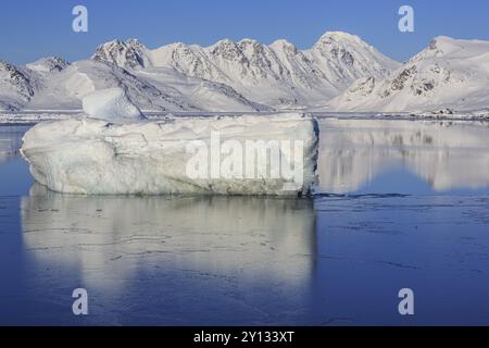 Iceberg nel fiordo di fronte a montagne innevate, soleggiato, invernale, artico, Kulusuk, Groenlandia orientale, Groenlandia, Nord America Foto Stock