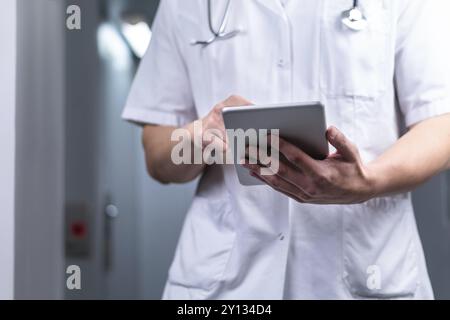 Foto di medico maschile in uniforme con stetoscopio che esce dall'ascensore e utilizzando tablet computer in ospedale. Concetto medico moderno Foto Stock