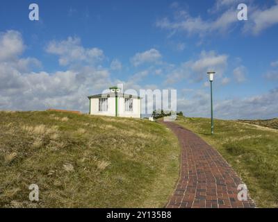 Una piccola casa bianca su una collina, accessibile tramite un sentiero in mattoni sotto un cielo blu con nuvole, spiekeroog, frisia orientale, mare settentrionale, germania Foto Stock