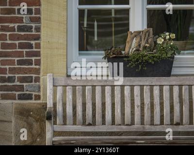 Una panchina di legno davanti a una finestra con fiori in una piantatrice sulla panchina, billerbeck, muensterland, germania Foto Stock