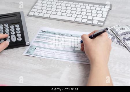 Punto di vista foto di donna e di calcolo e il riempimento di noi sotto forma di imposta accanto alla tastiera del computer e forma fiscale 1040. 15 aprile 2019 giornata fiscale Foto Stock