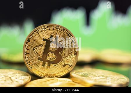 Una pila di monete d'oro Bitcoin davanti a un grafico di tendenza verde rialzista. Concetto di aumento dei prezzi Foto Stock