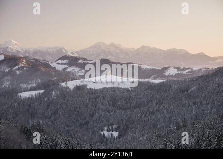 Bellissima alba paesaggio della Chiesa san Tommaso in Slovenia sulla collina nella nebbia mattutina con rosa e azzurro cielo e il monte Triglav sfondo Foto Stock