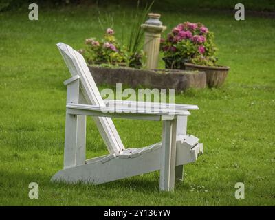 Una sedia di legno bianca si erge su un prato ben curato, sullo sfondo si trova un letto di fiori, spiekeroog, frisia orientale, mare del nord, germania Foto Stock