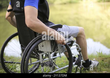 Uomo felice e giovane disabile o handicappato seduto su una sedia a rotelle in natura Foto Stock