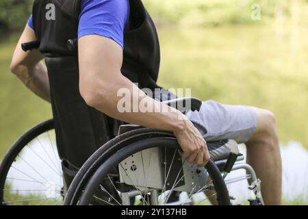 Uomo felice e giovane disabile o handicappato seduto su una sedia a rotelle in natura Foto Stock