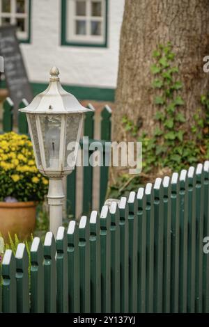 Lanterna bianca su una recinzione di legno verde con fiori gialli in vaso e albero con edera, spiekeroog, frisia orientale, mare del nord, germania Foto Stock