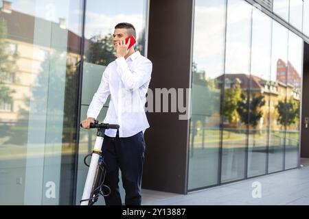 Giovani e casual uomo d affari di equitazione scooter elettrico e parlare sullo smartphone nella città Foto Stock