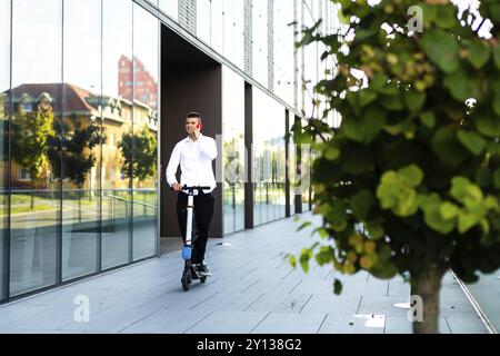 Giovani e casual uomo d affari di equitazione scooter elettrico e parlare sullo smartphone nella città Foto Stock