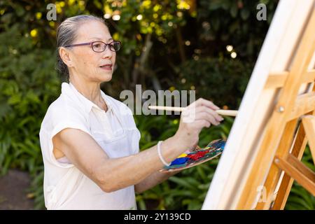 Pittura su tela, donna asiatica anziana che usa pennello e tavolozza in ambiente esterno Foto Stock