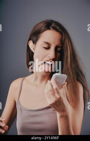 Una giovane donna possiede uno smartphone, che sembra disgustata da quello che legge, mostrando emozioni negative verso la tecnologia e i social media Foto Stock