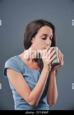 La giovane donna gode di un momento di pace con la sua tazza preferita, gli occhi chiusi per appagamento, assaporando una bevanda calda Foto Stock