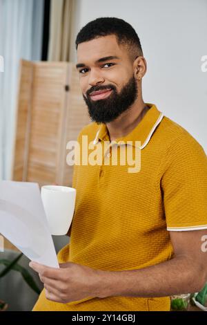 Un uomo sorridente con la barba sorseggia un caffè e rivede i giornali in un ambiente rilassato. Foto Stock