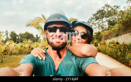 Primo piano giovane e felice coppia caucasica scatta selfie su smartphone mentre ti diverti a guidare uno scooter in un viaggio tropicale nel sud-est asiatico Foto Stock