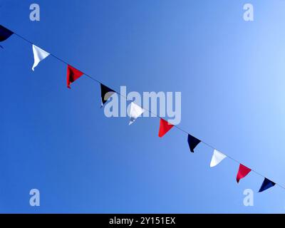 Le bandiere francesi triangolari in rosso, bianco e blu oscillano dolcemente contro un cielo blu vivace, migliorando l'atmosfera festosa di una festa Foto Stock