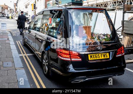 Un direttore funebre cammina di fronte a Un Black Hearse, High Street, Lewes, East Sussex, Regno Unito. Foto Stock