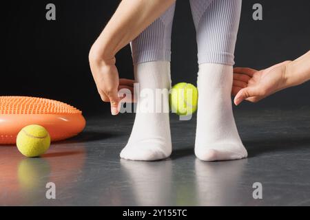 Rafforzando l'articolazione della caviglia con una palla da tennis, un terapista sta trattando le gambe, un massaggio ai piedi da vicino Foto Stock