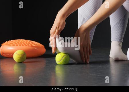 Rafforzando l'articolazione della caviglia con una palla da tennis, un terapista sta trattando le gambe, un massaggio ai piedi da vicino Foto Stock