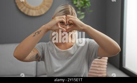 Donna bionda che crea una forma a cuore con le mani in un elegante salotto Foto Stock