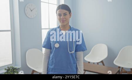 Una giovane e attraente donna ispanica in scrub si trova in una luminosa stanza d'ospedale. Foto Stock