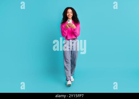 Foto a tutto il corpo di un'attraente ragazza adolescente che tiene il dispositivo che cammina vestiti eleganti rosa isolati su sfondo color acquamarina Foto Stock