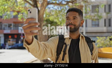 Un giovane afroamericano con la barba si fa un selfie all'aperto in un parco urbano, trasudando un'atmosfera informale e affascinante. Foto Stock