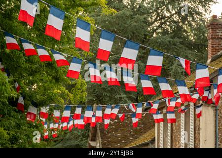 Disposizione di ghirlande di bandiera tricolore francese che decorano una strada di un villaggio in Francia. Concetti del giorno della Bastiglia e festa francese o evento patriottico Foto Stock