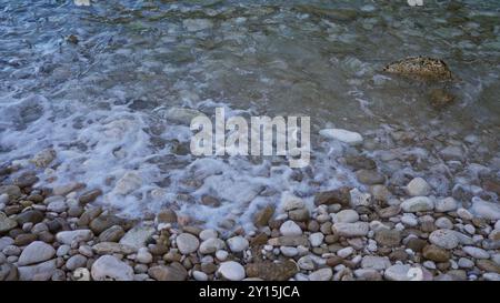 Litorale di ciottoli con onde dolci che scivolano sulle rocce in una giornata tranquilla e limpida che mostra una splendida scena costiera Foto Stock