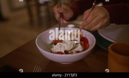 Un primo piano di una donna che gusta la fresca cucina italiana all'interno di un accogliente ristorante italiano, con una deliziosa insalata con pomodori ciliegini e burratto Foto Stock