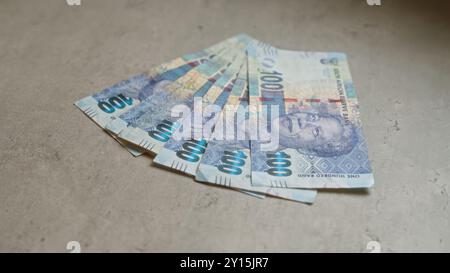 Le banconote sudafricane da 100 rand con mandela sono distribuite su una superficie di cemento Foto Stock