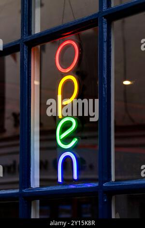 Colorato cartello al neon verticale con la parola "aperto" appeso all'interno di una vetrina, che indica che l'azienda è aperta ai clienti. newbiggin sul mare northumberland Foto Stock