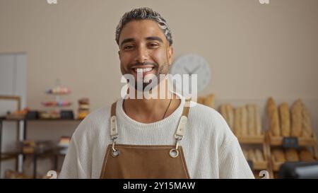 Bellissimo giovane arabo musulmano con una barba sorridente in un negozio interno di panetteria che indossa un grembiule Foto Stock