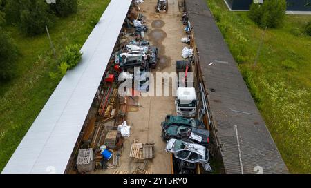 Vista aerea di un deposito di veicoli con varie auto smontate e parti sparse lungo un sentiero sterrato. L'area e' circondata dal verde e presenta un Foto Stock