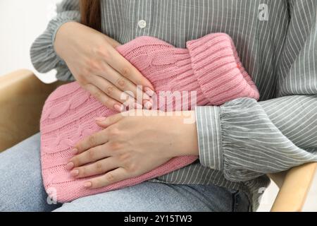 Donna che usa una bottiglia d'acqua calda per alleviare il dolore mestruale al chiuso, primo piano Foto Stock