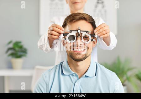 Felice e sorridente giovane che viene controllato dagli occhi con attrezzature speciali nell'ufficio dell'optometrista Foto Stock
