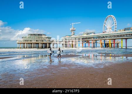 L'Aia, Paesi Bassi - 2 ottobre 2022: Una giovane coppia con tavola da surf in mano che cammina sulla spiaggia al molo di Scheveningen. Foto Stock