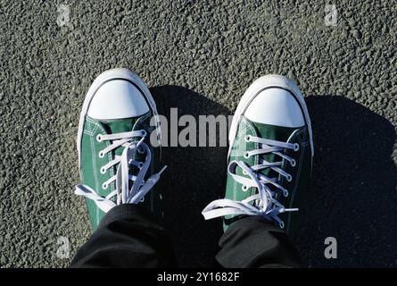 I piedi da uomo in sneaker verdi e bianche con lacci bianchi si stagliano sull'asfalto Foto Stock