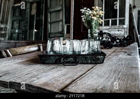Primo piano di tazze di vetro in vassoio di latta su un tavolo di fattoria in stile "Distressed" con lo sfondo di porte in legno al Farmhouse Style Store Foto Stock