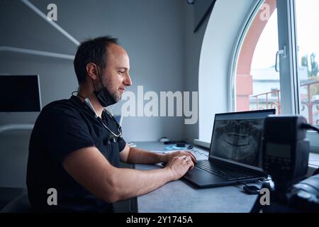 Il medico studia una radiografia della fila di denti su un computer portatile Foto Stock