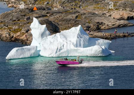 Nanortalik, Groenlandia - 27 agosto 2024: Turisti in motoscafo che attraversano un grande iceberg fuori dal porto di Nanortalik, con gente sulle rocce Foto Stock