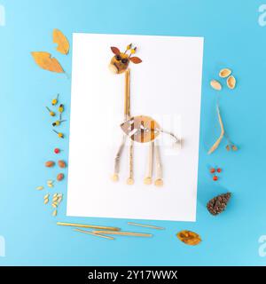 Artigianato autunnale per bambini, giraffa fatta di foglie. Grande foglia marrone con macchie bianche per il corpo, foglie più piccole per la testa, foglie gialle come orecchie, ramoscelli come antenne Foto Stock