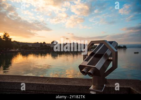 Binocolo a gettoni o telescopio per turisti. Alba estiva, cielo spettacolare, acqua del lago e edifici sullo sfondo, profondità di campo ridotta, Foto Stock