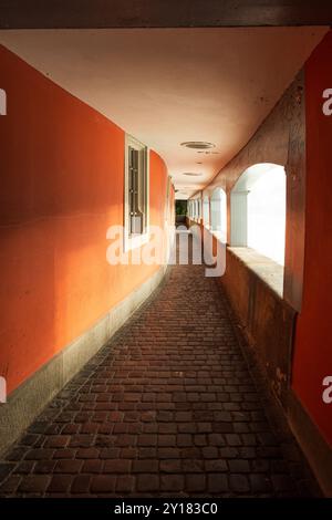 Passaggio pedonale o corridoio vecchio e vuoto in una città europea. Parete arancione brillante, luce del sole che passa attraverso gli archi, nessuna gente. Foto Stock